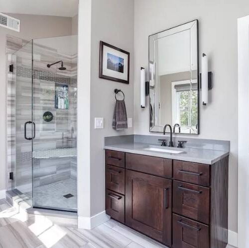 Modern bathroom design featuring dark wood cabinetry, sleek countertop, large mirror, and glass shower enclosure with tiled walls, emphasizing BKC Kitchen and Bath's stylish cabinetry options for home renovations.