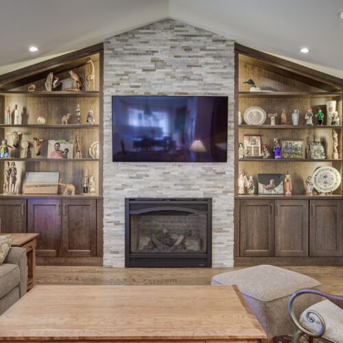 Living room featuring a stone accent wall with a mounted television, flanked by wooden cabinetry displaying decorative items and a cozy fireplace, emphasizing stylish interior design for home aesthetics.