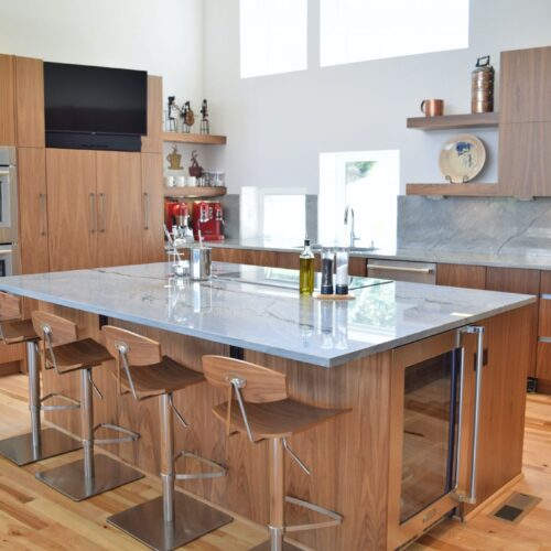 Modern kitchen design featuring a spacious island with a marble countertop, wooden cabinetry, stainless steel appliances, and contemporary bar stools, showcasing BKC Kitchen and Bath's innovative kitchen remodeling expertise.