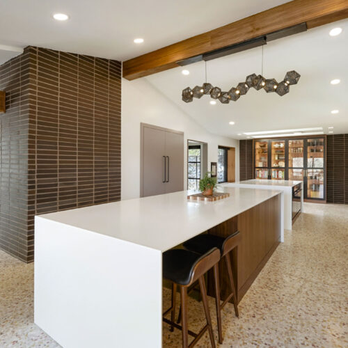 Modern kitchen design featuring a large white island with wooden accents, sleek cabinetry, and contemporary pendant lighting, showcasing innovative remodeling by BKC Kitchen and Bath.