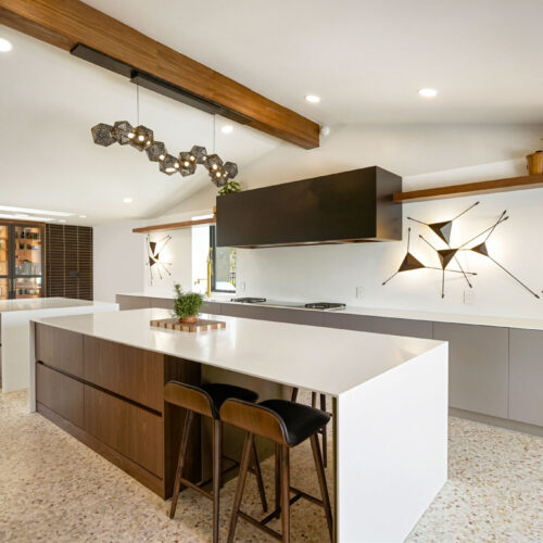 Modern kitchen design featuring an island with a white countertop, dark wood cabinetry, stylish pendant lighting, and contemporary wall art, showcasing BKC Kitchen and Bath's innovative remodeling services.