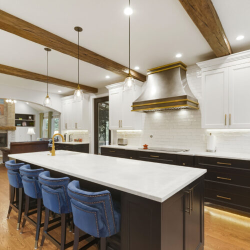 Modern kitchen design featuring white cabinetry, a large island with blue upholstered bar stools, and a decorative range hood, showcasing BKC Kitchen and Bath's innovative remodeling services.