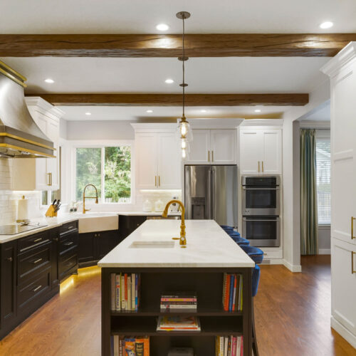 Modern kitchen design featuring a large island with bookshelves, black cabinetry, marble countertops, stainless steel appliances, and wooden beams, showcasing BKC Kitchen and Bath's innovative remodeling style.