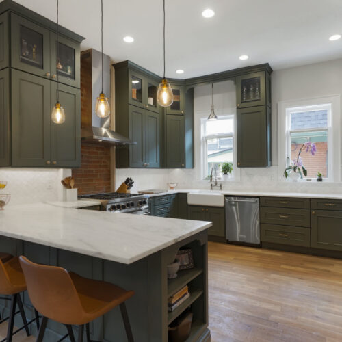 Modern kitchen design featuring dark green cabinetry, white marble countertops, pendant lighting, and stainless steel appliances, showcasing a blend of functionality and style in a welcoming environment.
