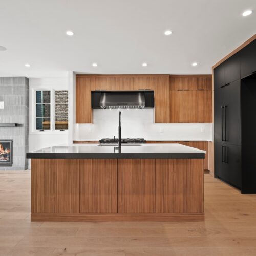 Modern kitchen design featuring a central island with a dark countertop, wooden cabinetry, and stainless steel appliances, showcasing a blend of contemporary and transitional styles.