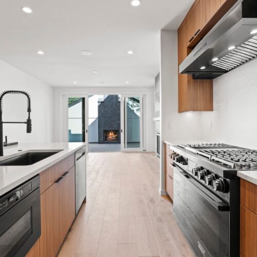 Modern kitchen design featuring sleek cabinetry, stainless steel appliances, and an open layout with a view of an outdoor fireplace.