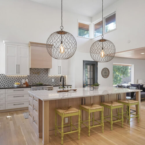 Modern kitchen design featuring a spacious island with light wood cabinetry, vibrant green bar stools, and decorative pendant lighting, showcasing innovative cabinetry and exceptional craftsmanship by BKC Kitchen and Bath.