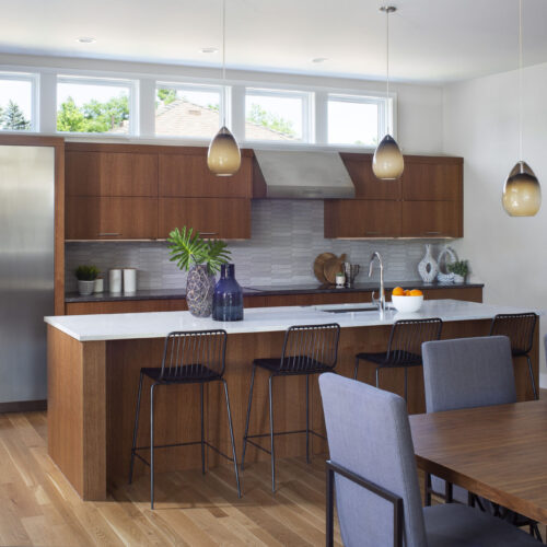 Modern kitchen design featuring wooden cabinetry, a white countertop, bar stools, and decorative elements, highlighting BKC Kitchen and Bath's innovative remodeling services.