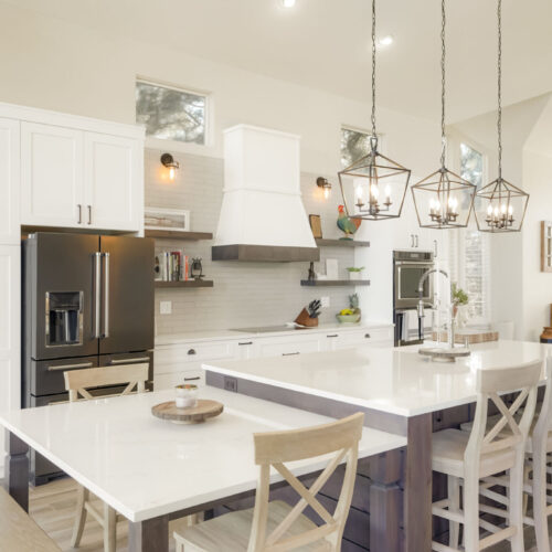 Modern kitchen featuring white cabinetry, a central island with a quartz countertop, pendant lighting, and stainless steel appliances, showcasing a blend of functionality and contemporary design.