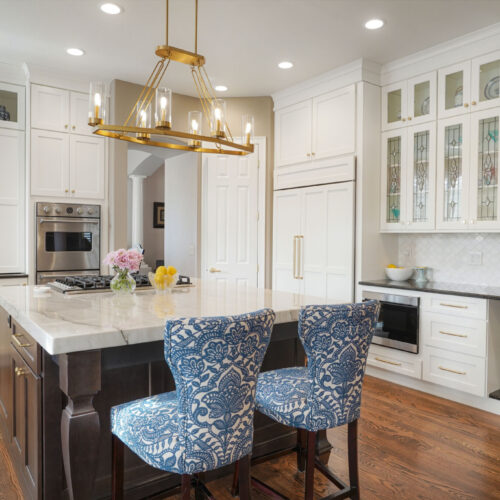Modern kitchen design featuring white shaker cabinets, a marble countertop island, and blue patterned chairs, illuminated by a stylish chandelier, showcasing an elegant and functional space for cooking and entertaining.
