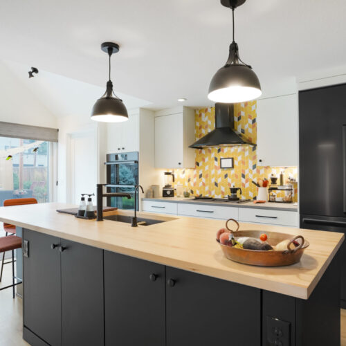 Modern kitchen featuring black cabinetry, a light wood island countertop, and stylish pendant lighting, with a patterned backsplash and contemporary appliances, showcasing a blend of functionality and design.