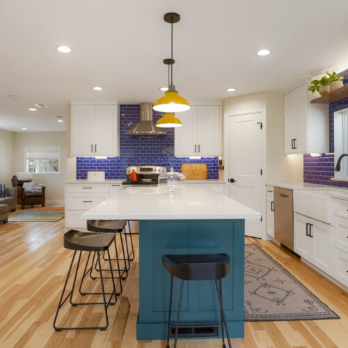 North Raleigh blue kitchen featuring white cabinetry, a teal kitchen island with bar stools, yellow pendant lights, and a backsplash of blue tiles, showcasing modern design elements for kitchen inspiration.