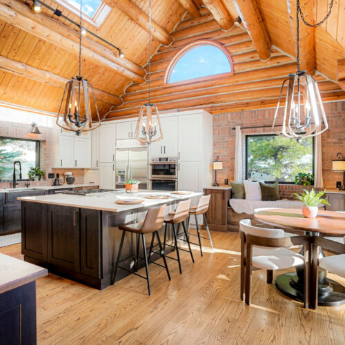 North October Place Mountain Kitchen featuring modern white shaker cabinets, a spacious island with seating, rustic wooden beams, and large windows for natural light.