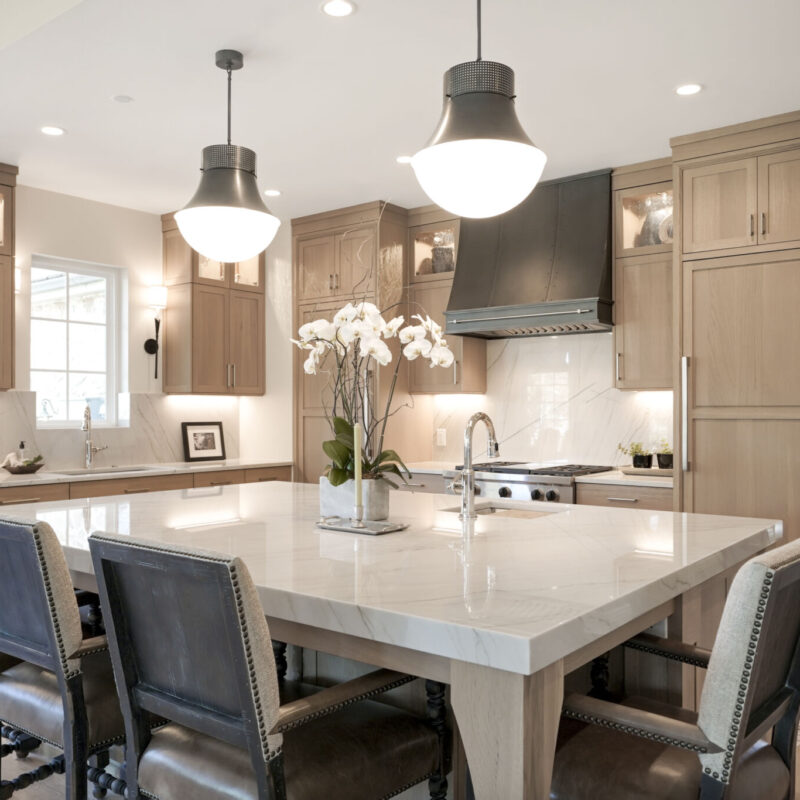BKC Kitchen and Bath transitional kitchen with light wood cabinets, large center island and metal pendant lights
