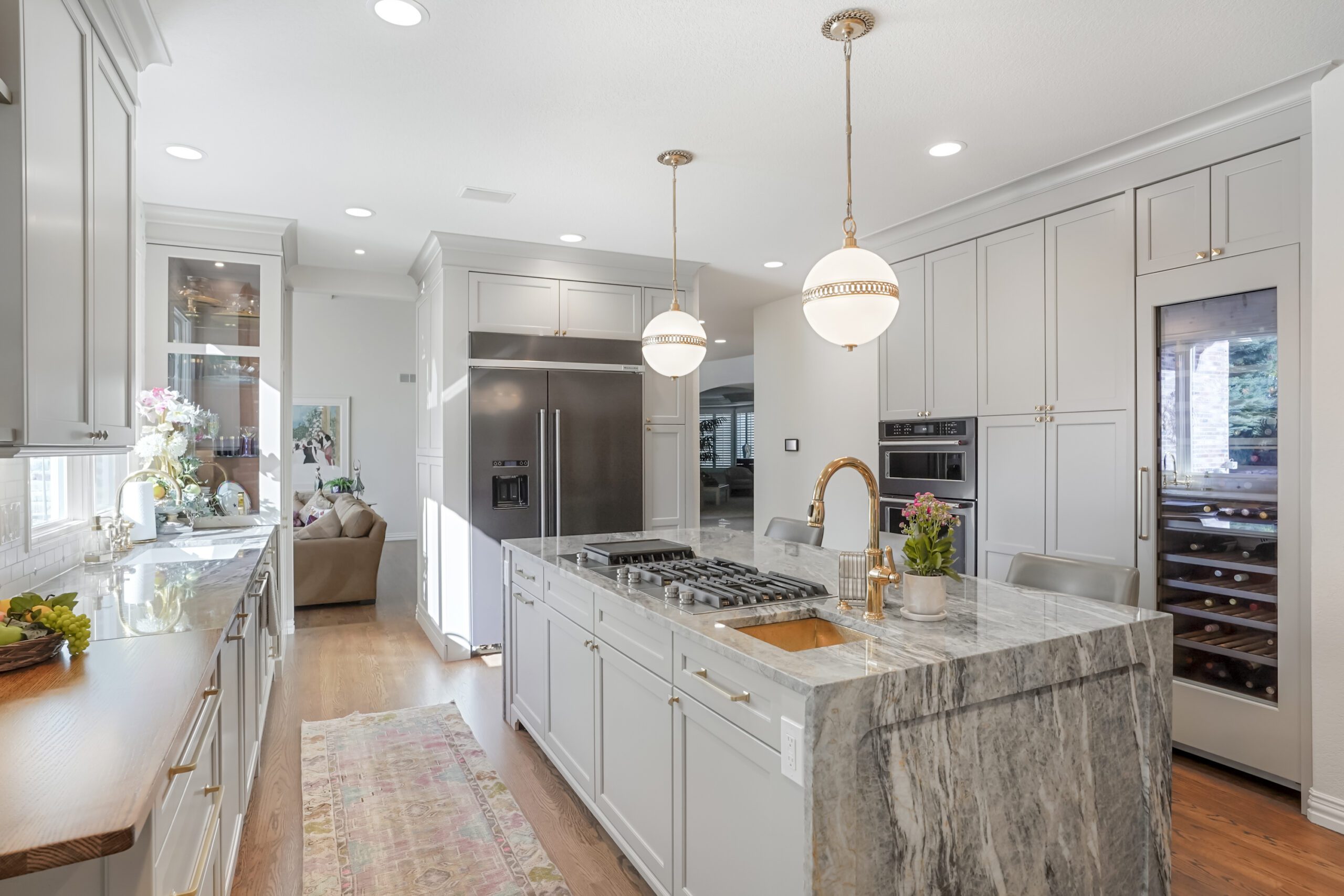 Modern kitchen with gray cabinetry, marble countertop, stainless steel appliances, pendant lighting, and a wine cooler, showcasing BKC Kitchen and Bath's elegant design and functionality.