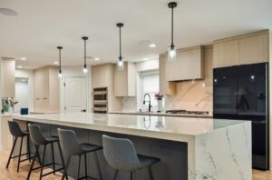 Modern kitchen design featuring a large island with a 6CM countertop and dual waterfall edges, complemented by stylish bar stools, sleek cabinetry, and contemporary pendant lighting, showcasing BKC Kitchen & Bath's cabinetry expertise.