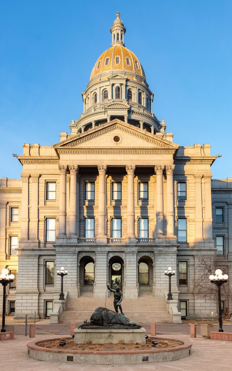 Denver Capitol building with a golden dome, featuring a statue in the foreground and surrounded by lampposts, representing Congress Park's historic architecture.